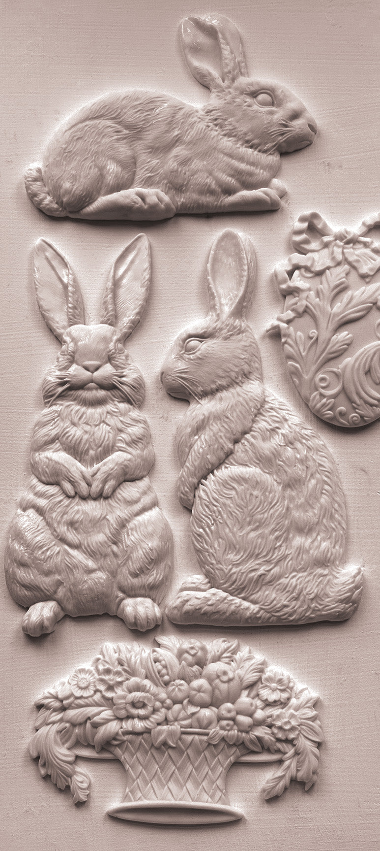 Close up of white castings from iron Orchid Designs Les Lapins mould. Three white clay rabbits, a basket and an egg on a white background.
