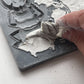 A close up image of a hand removing excess clay from Iron Orchid Designs Specimens mould