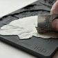 Hand using a ruler to scrape out excess clay from Iron Orchid Designs Spring Garden grey silicone mould