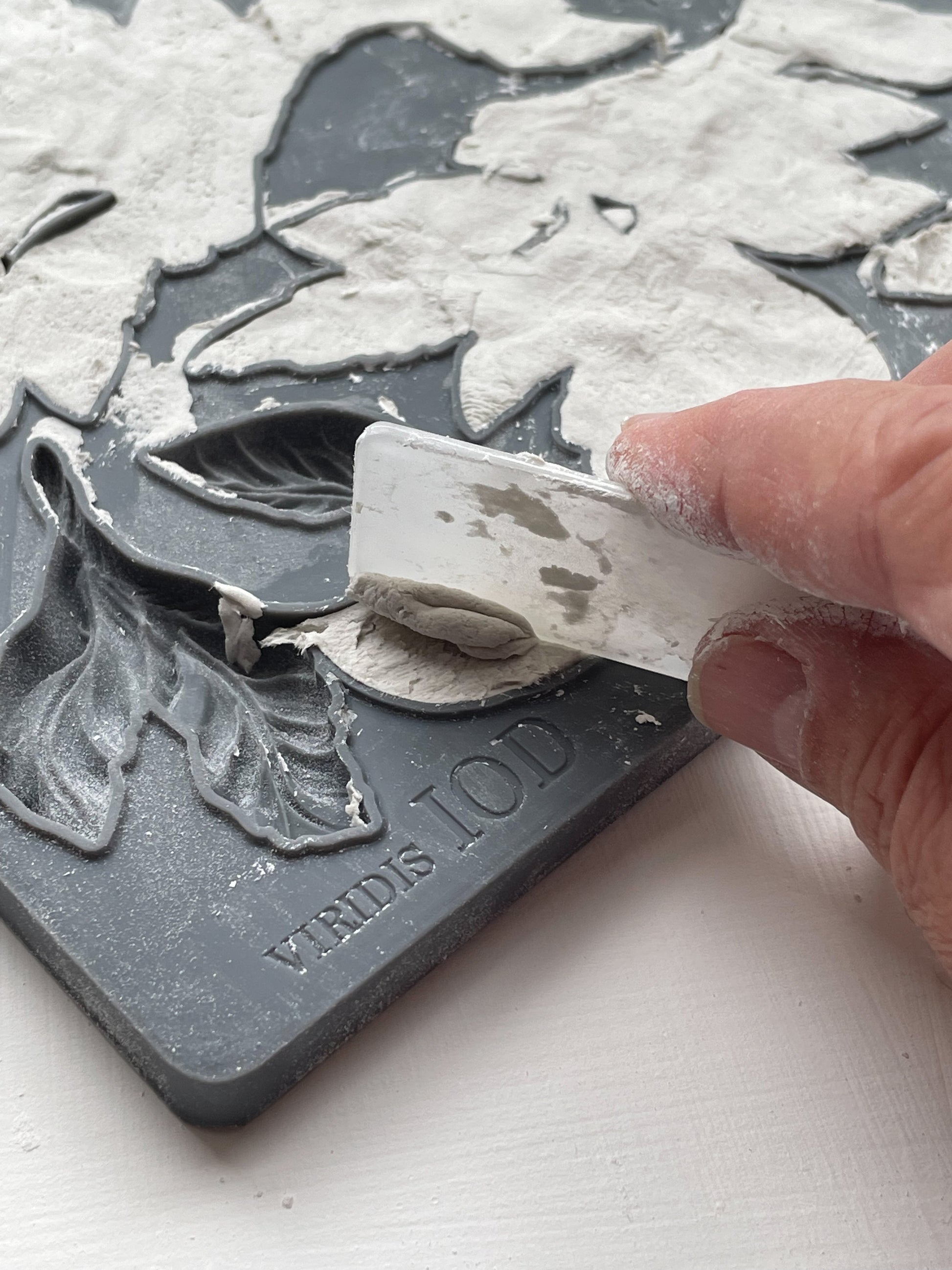 A close up image of a hand removing excess clay from iron Orchid Designs Viridis mould