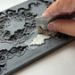 Person using a tool to remove excess air dry clay from a decorative mould with intricate designs from Iron Orchid Designs