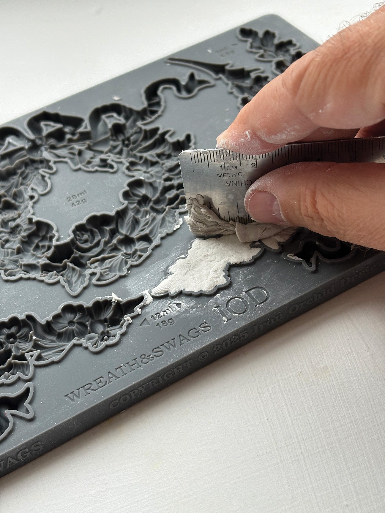 Person using a tool to remove excess air dry clay from a decorative mould with intricate designs from Iron Orchid Designs