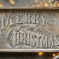 Decorative wooden tray with 'Merry Christmas' text on a wooden surface with lights and greenery by Iron Orchid Designs