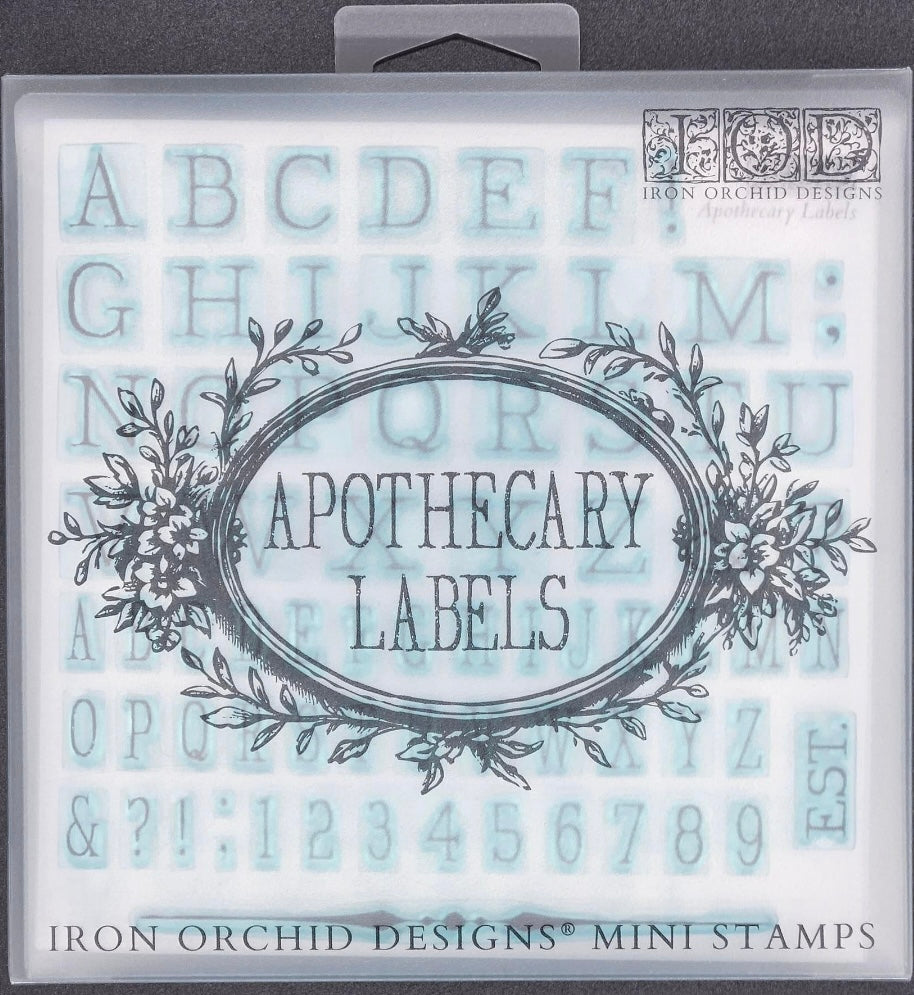 A photograph of the front of the box for Iron Orchid Designs Apothecary Labels Stamp. The image shows the name of the stamps and some of the letters of the alphabet stamps can be seen in the background