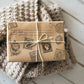 A prersent wrapped in brown paper which has been stamped with Ephemeral Type Stamp from Iron Orchid Designs. The parcel is tied with white string and is standing on a woollen blanket