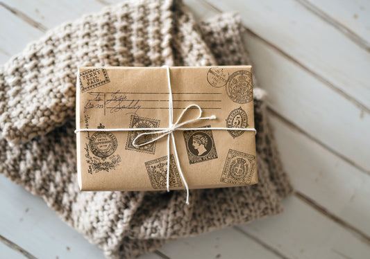A prersent wrapped in brown paper which has been stamped with Ephemeral Type Stamp from Iron Orchid Designs. The parcel is tied with white string and is standing on a woollen blanket