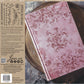 Pink notebook stamped Iron Orchid Designs Flora and Vine with floral patterns on a rustic background