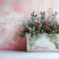 Decorative floral arrangement with red berries in a stamped wooden box against a pink textured background