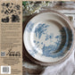 Decorative stamped plate with blue bird design on a rustic wooden surface, surrounded by nature-themed elements.