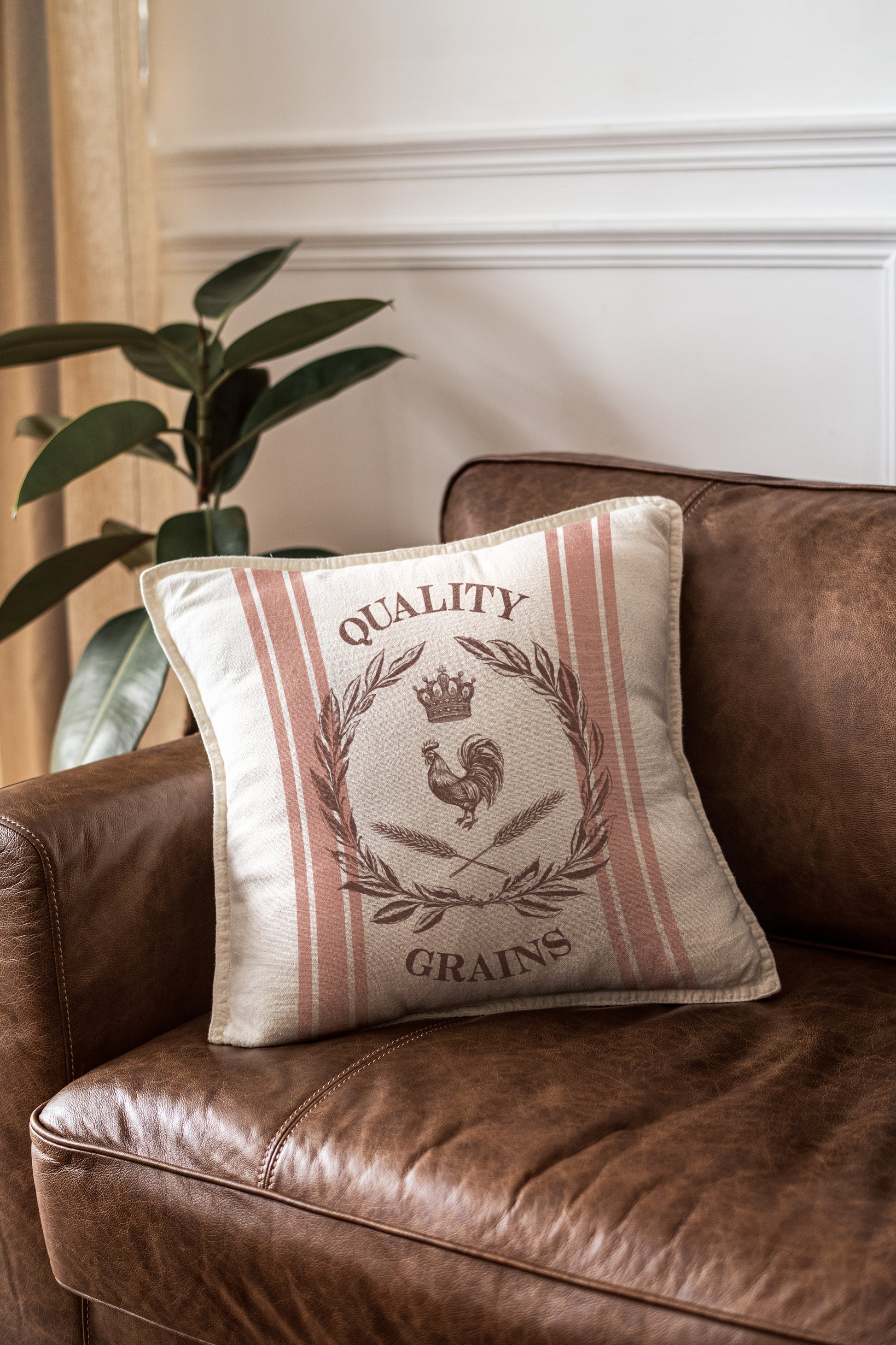 A striped cushion that has been stamped with a grain sack effect using stamps from Iron Orchid Designs Mercantile stamp. The cushion has been placed on a tan leather chair and is next to a large leaved plant.