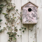 Decorative birdhouse with floral pattern on a white wooden wall with climbing plants from Iron Orchid Designs Nature's Etchings stamp.