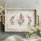 Decorative tray with floral design and bird illustration on a light gray surface with flowers around.