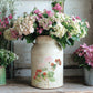 Vintage milk churn with floral arrangement surrounded by potted flowers on a rustic wooden surface from Iron Orchid Designs Marche des Fleurs