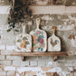 Decorative cutting boards with floral and rooster designs on a rustic shelf against a brick wall by Iron Orchid Designs