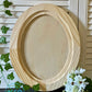 Wooden oval craft blank on a surface with greenery and flowers in the background by Iron Orchid Designs