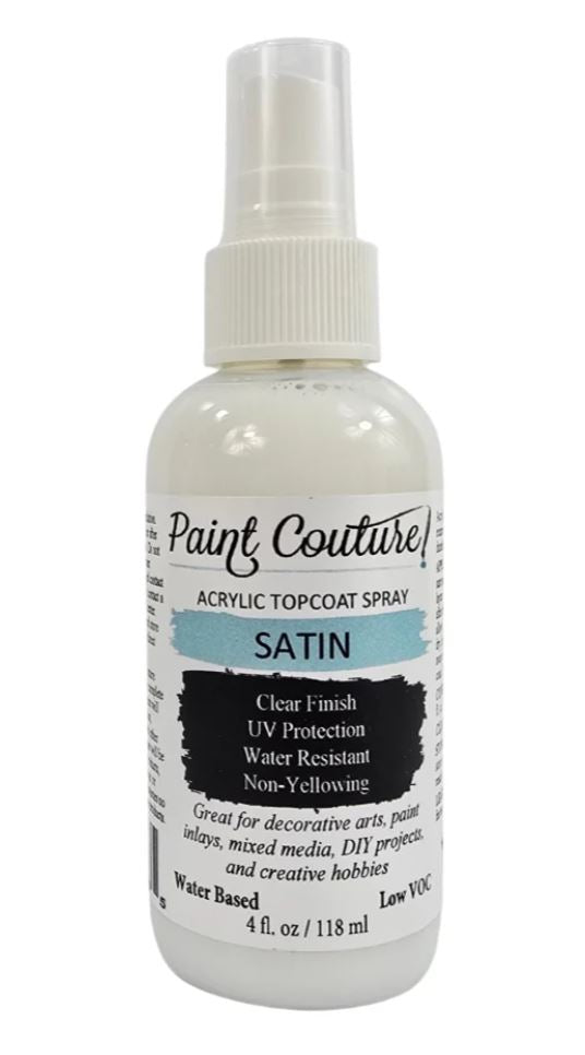 A bottle of Paint Couture Acrylic Topcoat Spray in the satin finish, featuring a white spray nozzle and a label with white, black, and light blue text.