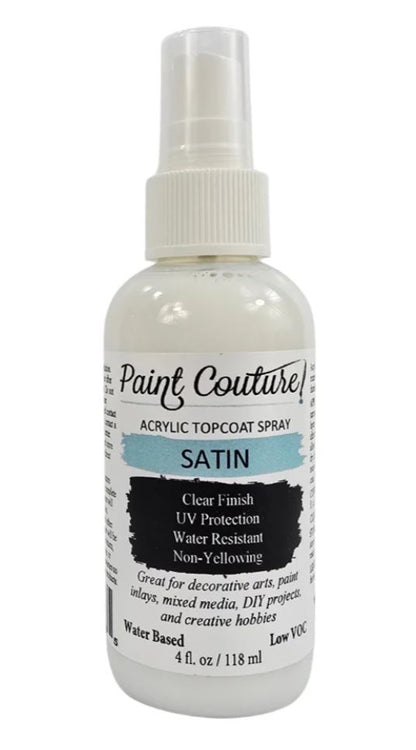 A bottle of Paint Couture Acrylic Topcoat Spray in the satin finish, featuring a white spray nozzle and a label with white, black, and light blue text.