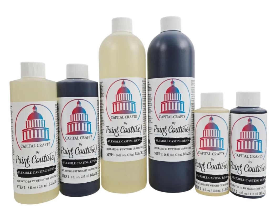 A set of six Capital Crafts by Paint Couture Flexible Casting Resin bottles in various colors, including black, dark blue, and cream, arranged against a plain white background.