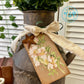 Decorative rusty milk churn with a floral tag and bow, featuring a rustic design.