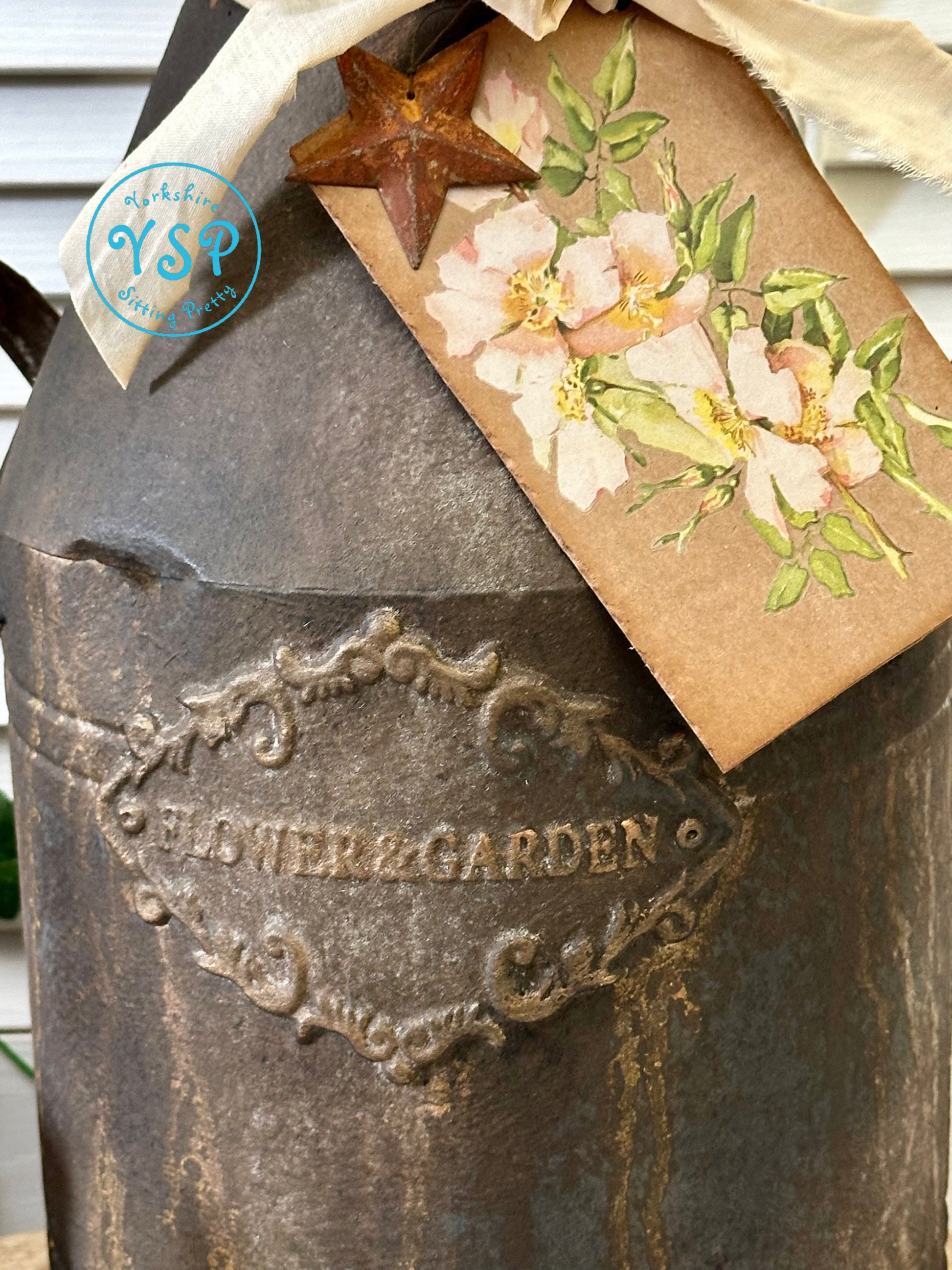 Decorative rusty milk churn with floral tag and star detail