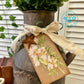 Decorative rusty milk churn with greenery, ribbon, and floral tag on a neutral background
