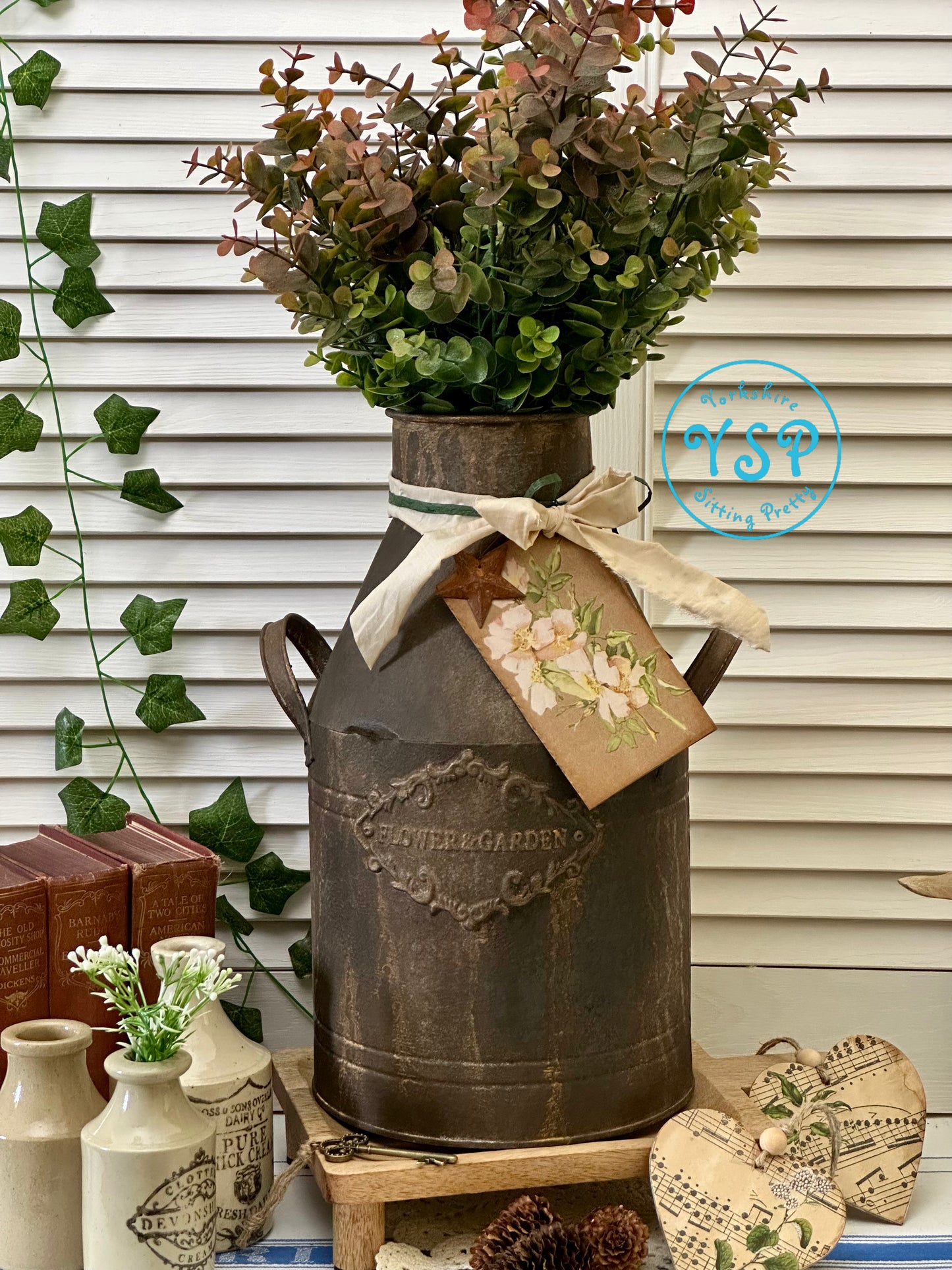 Decorative rusty milk churn with flowers and a tag on a white wall background