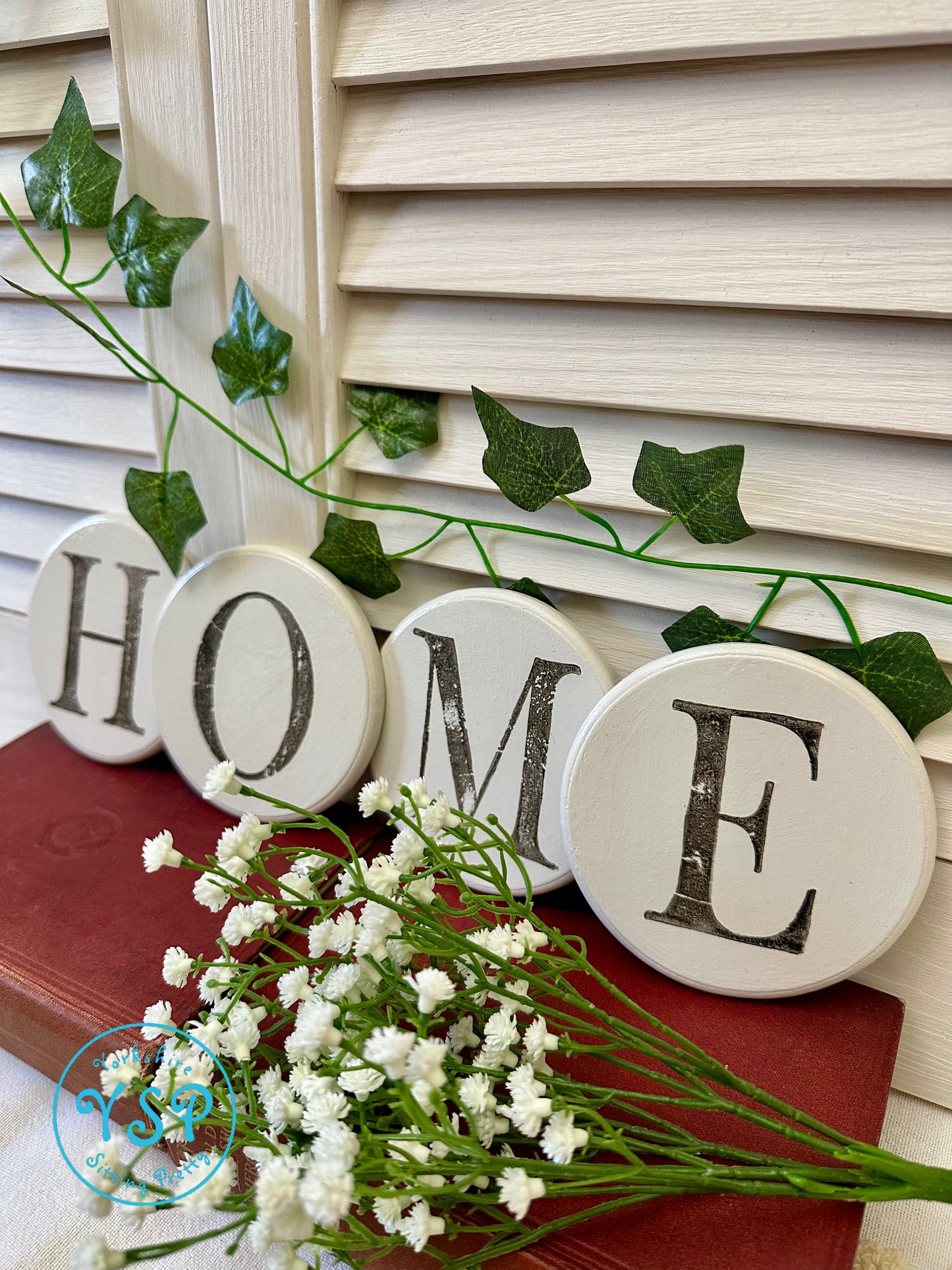 Four white round coasters painted white spelling out home set against a white background on a red surface