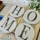 Four round white coasters with letters spelling 'HOME' on a open book background.