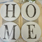 Decorative white round coasters spelling 'HOME' on a book with flowers and doily.
