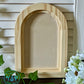 Wooden arch-shaped crafting blank on a wooden surface with flowers and leaves by Iron Orchid Designs