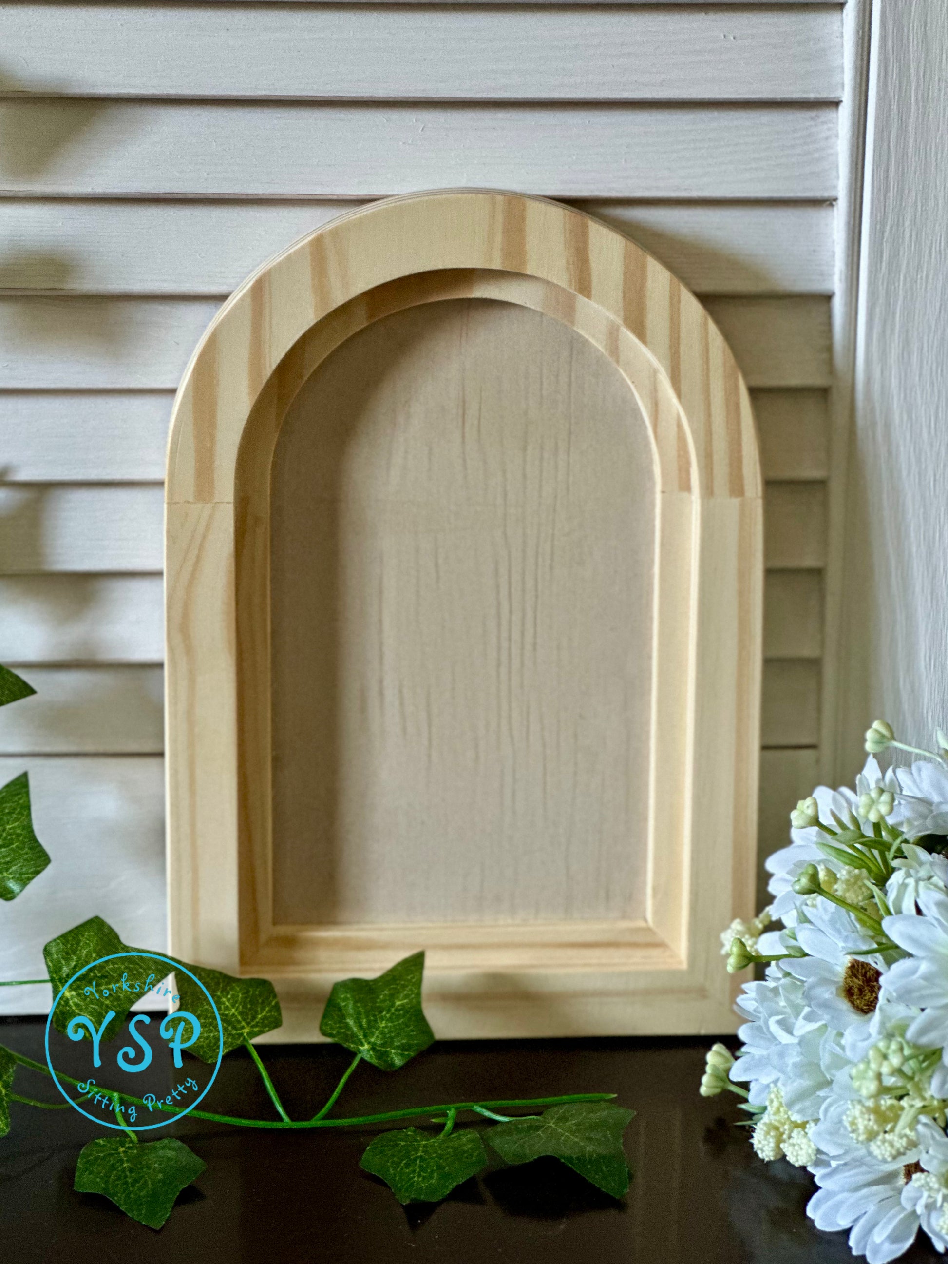 Wooden arch-shaped crafting blank on a wooden surface with flowers and leaves by Iron Orchid Designs