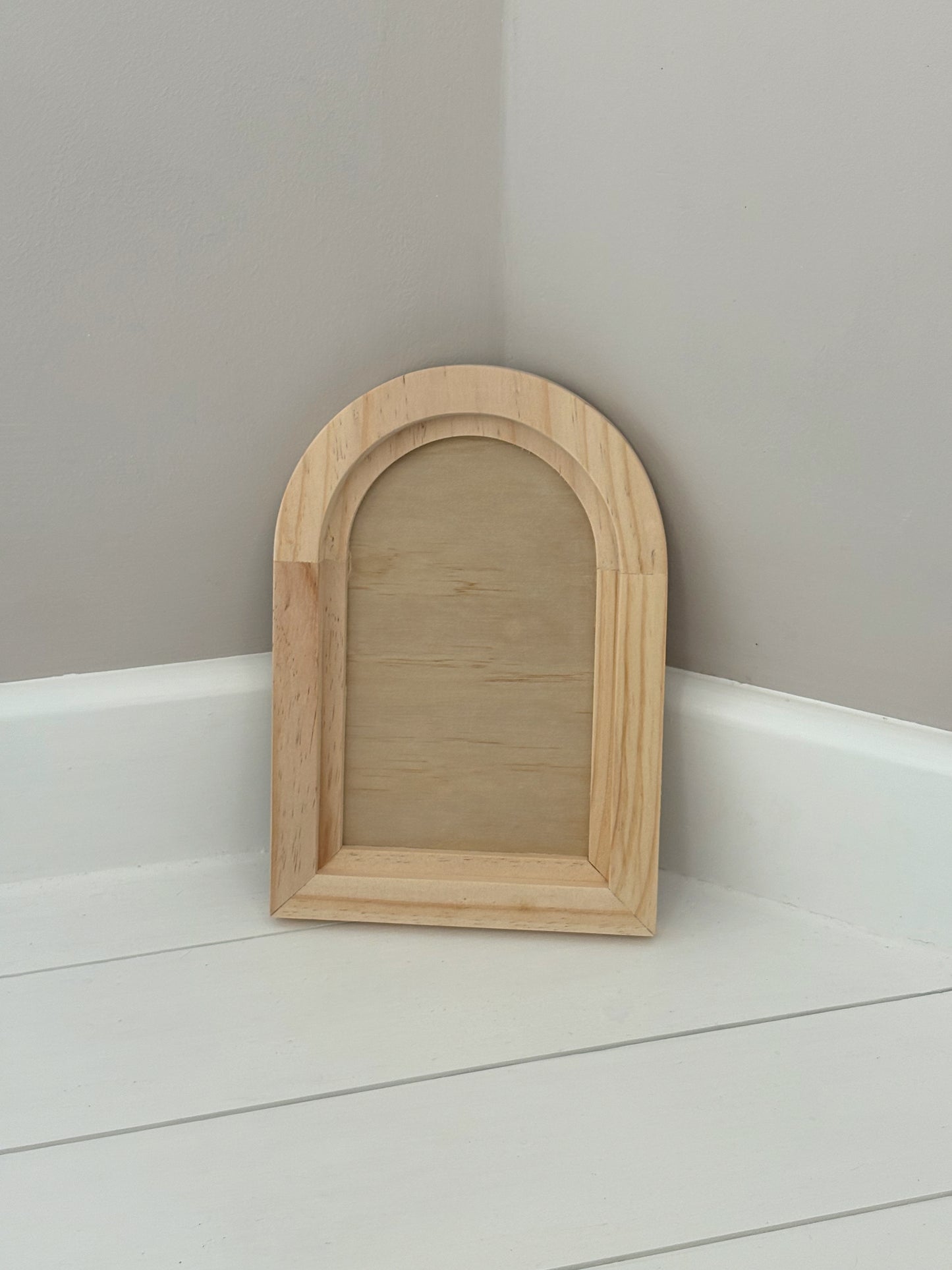Wooden arch-shaped crafting blank on a white surface with a grey wall by Iron Orchid Designs 