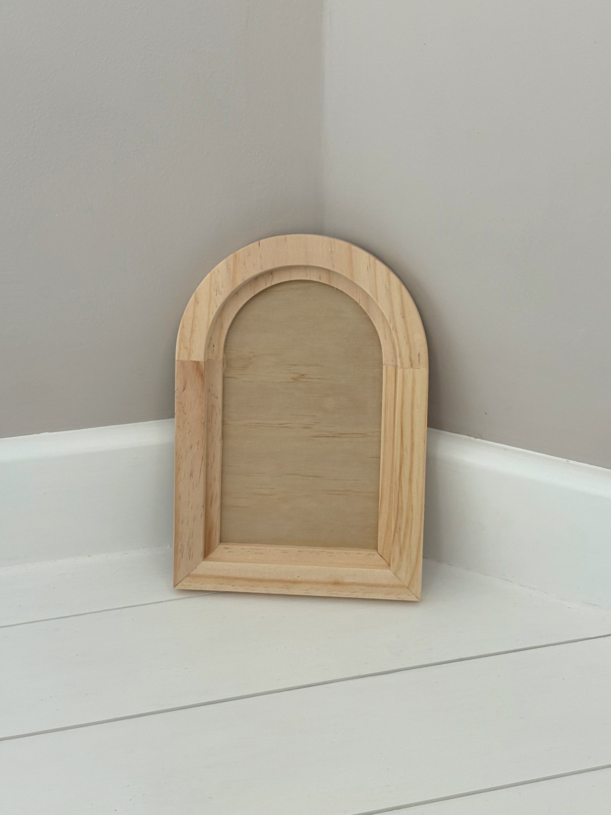 Wooden arch-shaped crafting blank on a white surface with a grey wall by Iron Orchid Designs 