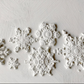 White embossed snowflake wall decals arranged on a textured white plaster background. Snowflakes by Iron Orchid Designs