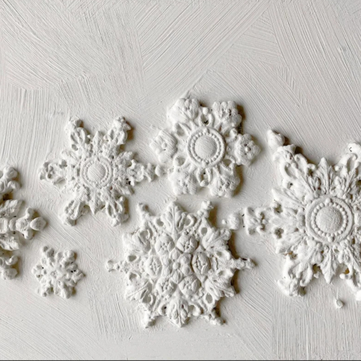 White embossed snowflake wall decals arranged on a textured white plaster background. Snowflakes by Iron Orchid Designs