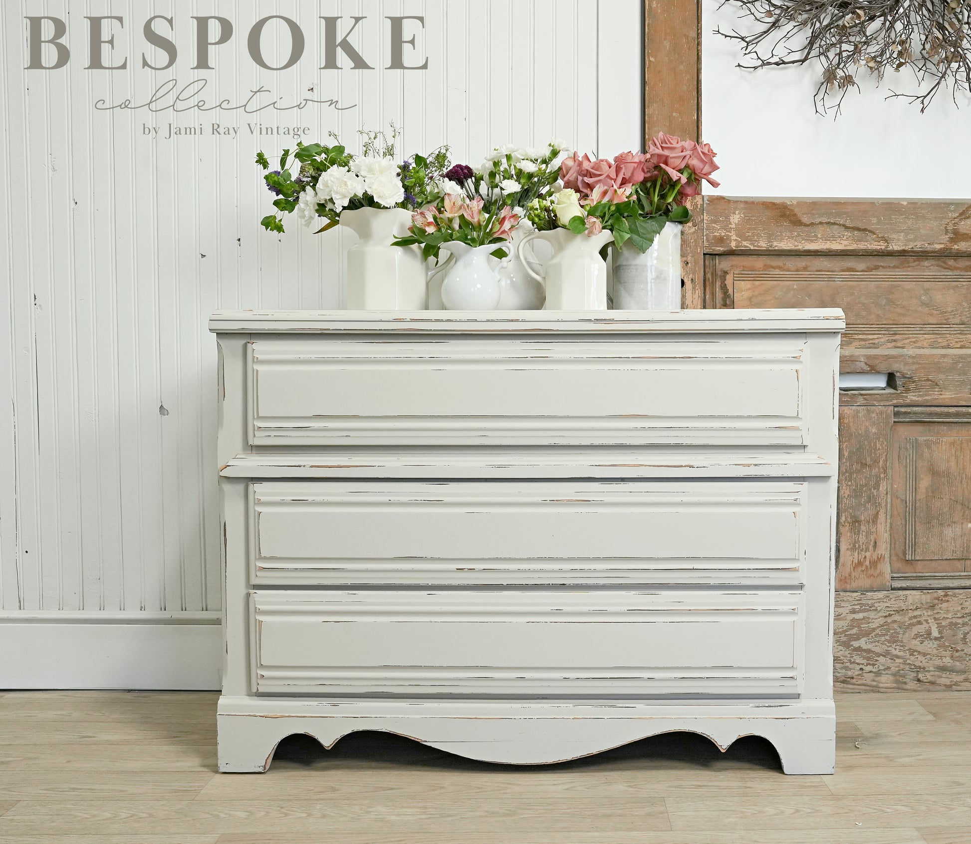 Vintage-style chest of drawers painted with Sweet Pickins Antique Ironstone Milk Paint with floral arrangements on top against a rustic wooden wall.