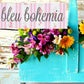 Colorful flowers in a blue vase with 'bleu bohemia' sign above on wooden background