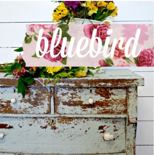 Vintage wooden chest with floral arrangement and 'bluebird' sign on a white wooden background