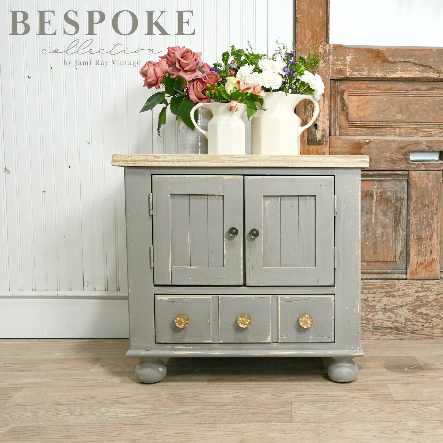 Gray cabinet with wooden top and floral arrangements on a wooden floor.