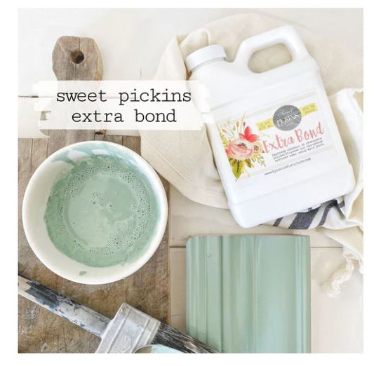 Sweet Pickins Extra Bond product with a bowl of green milk paint and a brush on a wooden surface.