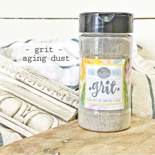 Container labelled 'SWeet Pickins grit aging dust' on a wooden surface with decorative elements in the background.