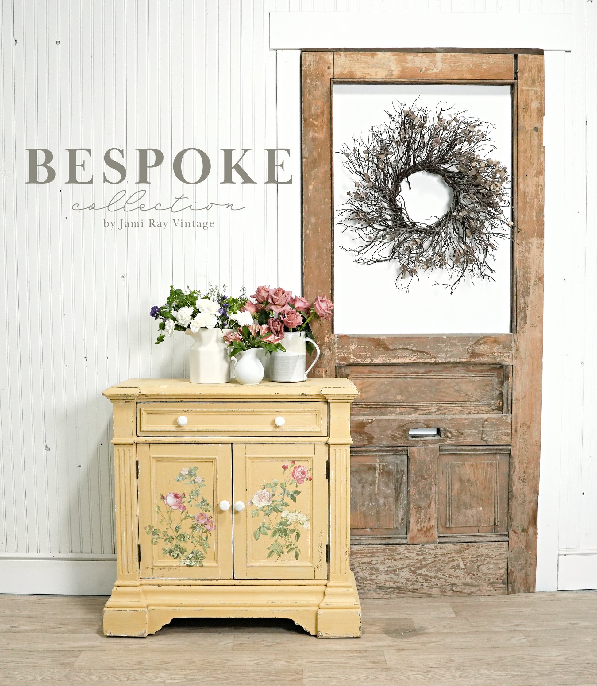Vintage-style cabinet with floral design in a room with a wooden door and wreath.