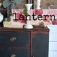 Decorative lantern with floral design and 'Lantern' text on a wooden surface.