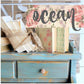 Decorative setup with books and a floral sign on a blue wooden surface.