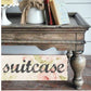Wooden suitcase with decorative items on top and a floral 'suitcase' sign below.