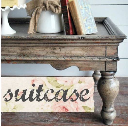 Wooden suitcase with decorative items on top and a floral 'suitcase' sign below.