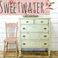 Vintage-style dresser with a pink chair against a white wooden wall with floral accents.