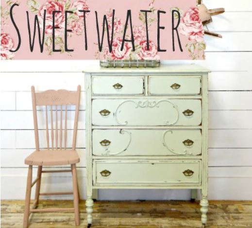 Vintage-style dresser with a pink chair against a white wooden wall with floral accents.