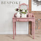 Pink vanity table with flowers and decor against a wooden wall, featuring 'Bespoke Collection' text.