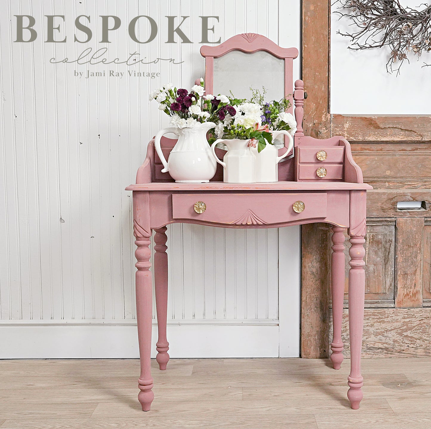 Pink vanity table with flowers and decor against a wooden wall, featuring 'Bespoke Collection' text.